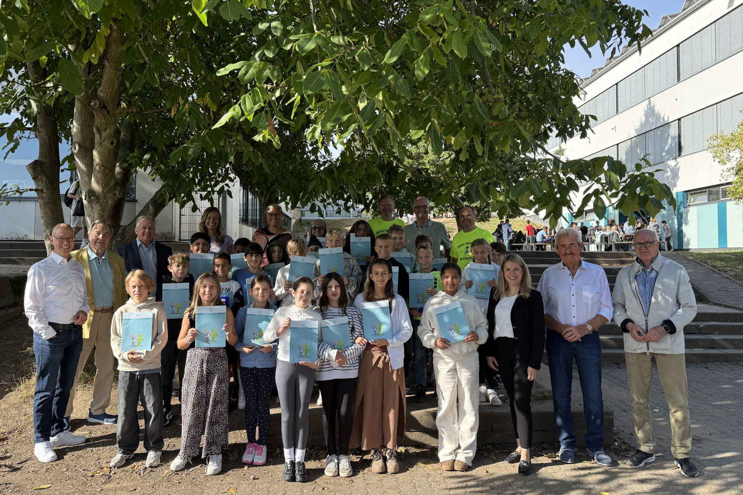 Gruppenfoto an der Bertha-von-Suttner-Schule Nidderau: Schülerinnen und Schüler der fünften Klassen präsentieren ihre Arbeitshefte zum Methodentraining „Lernen lernen“. Gemeinsam mit Vertreterinnen und Vertretern der Schulleitung, des Fördervereins und der Bürgerstiftung stehen sie auf dem Schulgelände unter einem großen Baum.