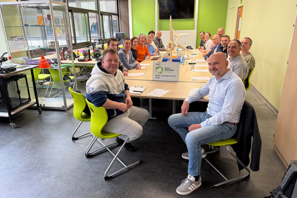 Eine Gruppe von Menschen sitzt an einem langen Tisch im MINT-Zentrum Eschborn zu einer Netzwerksitzung für MINT-Bildung.